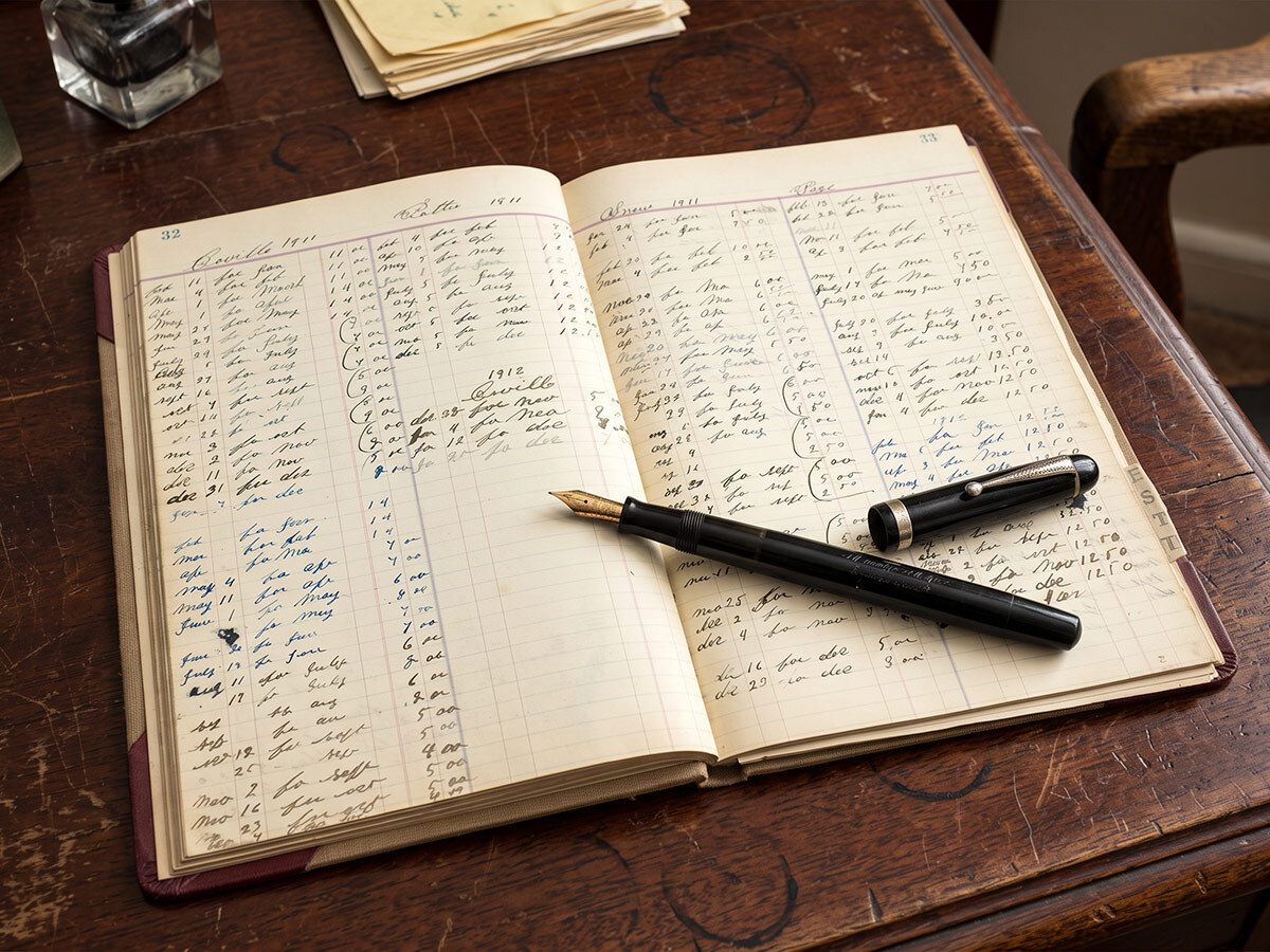 An old handwritten ledger open on a desk with a fountain pen